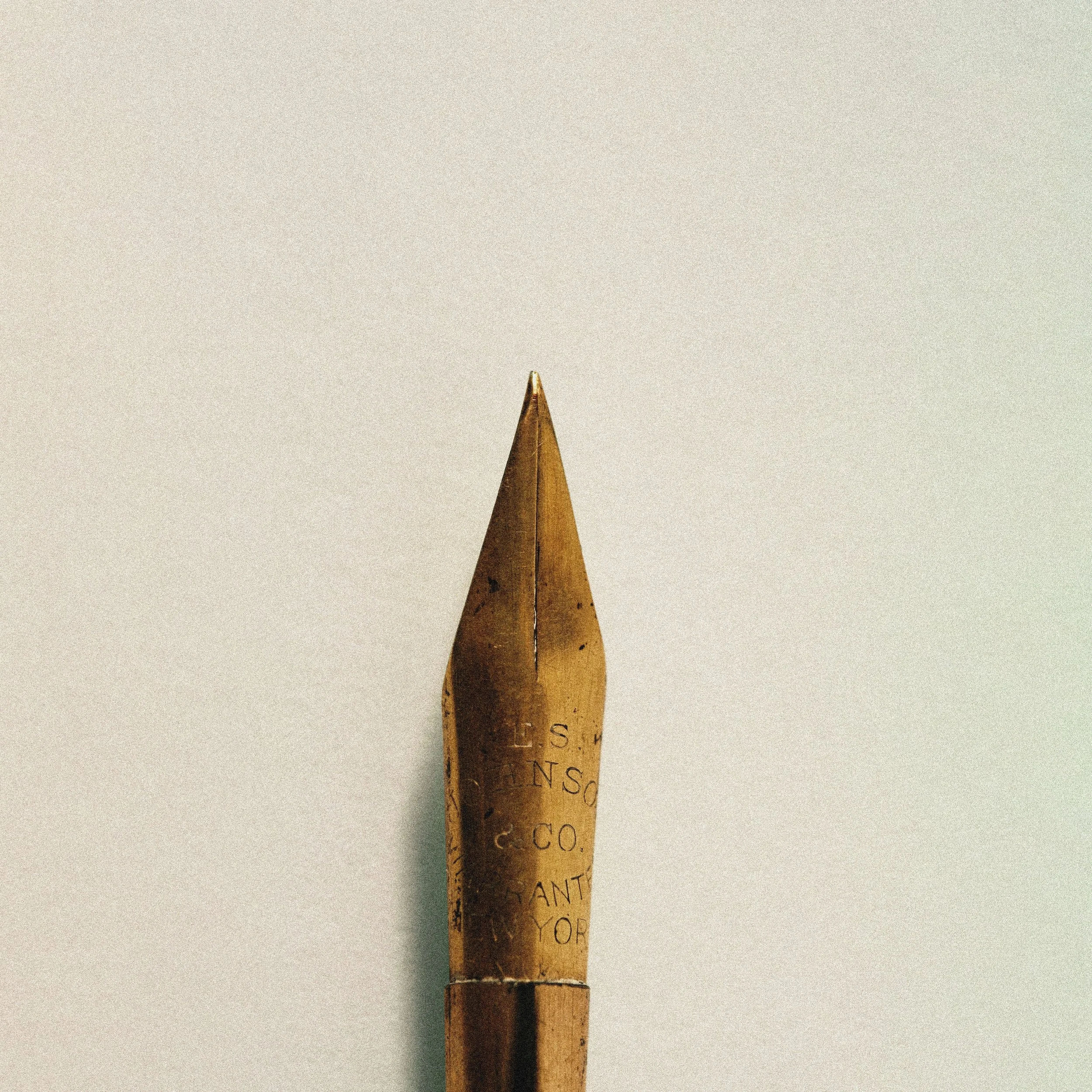 Close-up of a vintage fountain pen nib against a plain background.