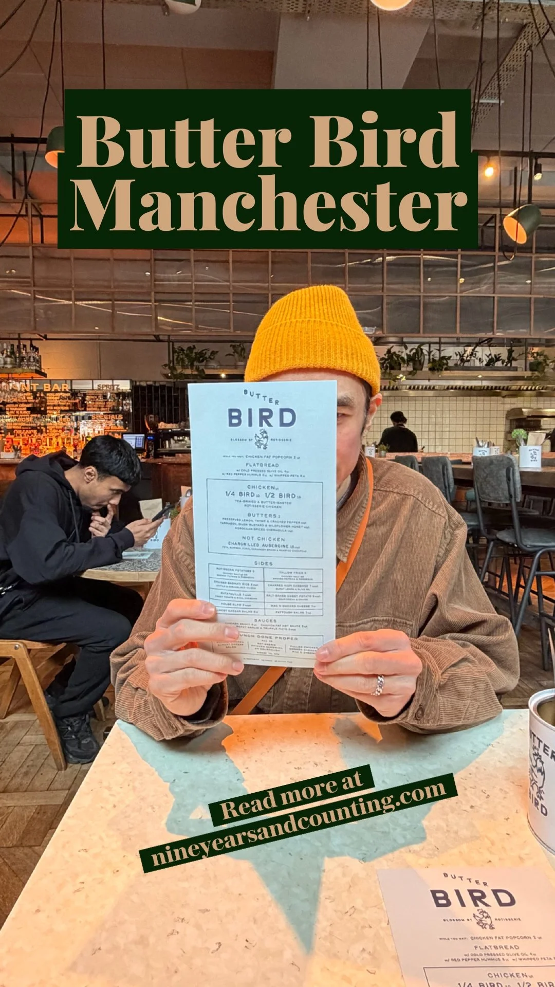 A person in a yellow beanie holding up a menu at Butter Bird Manchester restaurant, with a sign reading 'Read more at nineyearsandcounting.com' superimposed on the image. The restaurant interior has a modern design with people dining and a bar in the background.
