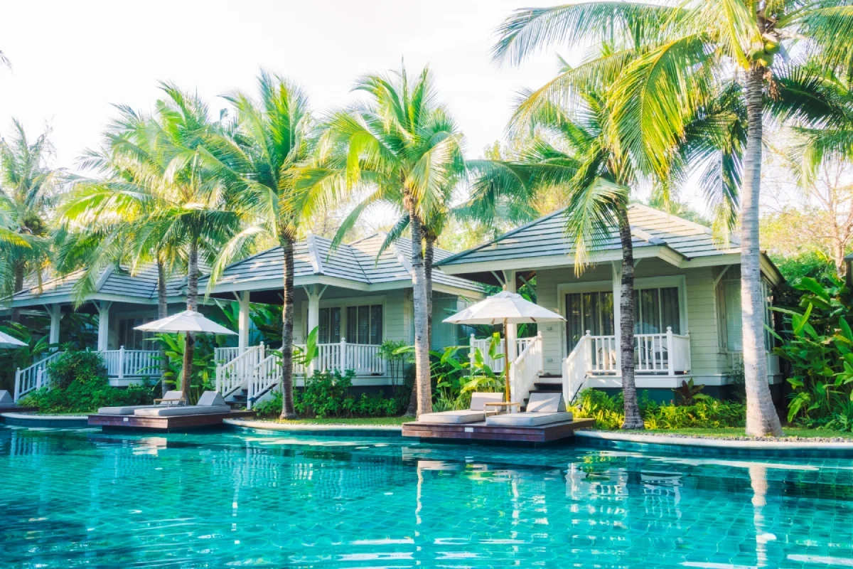 Luxury resort with bungalow-style cottages, palm trees, and a large swimming pool with lounge chairs and umbrellas.