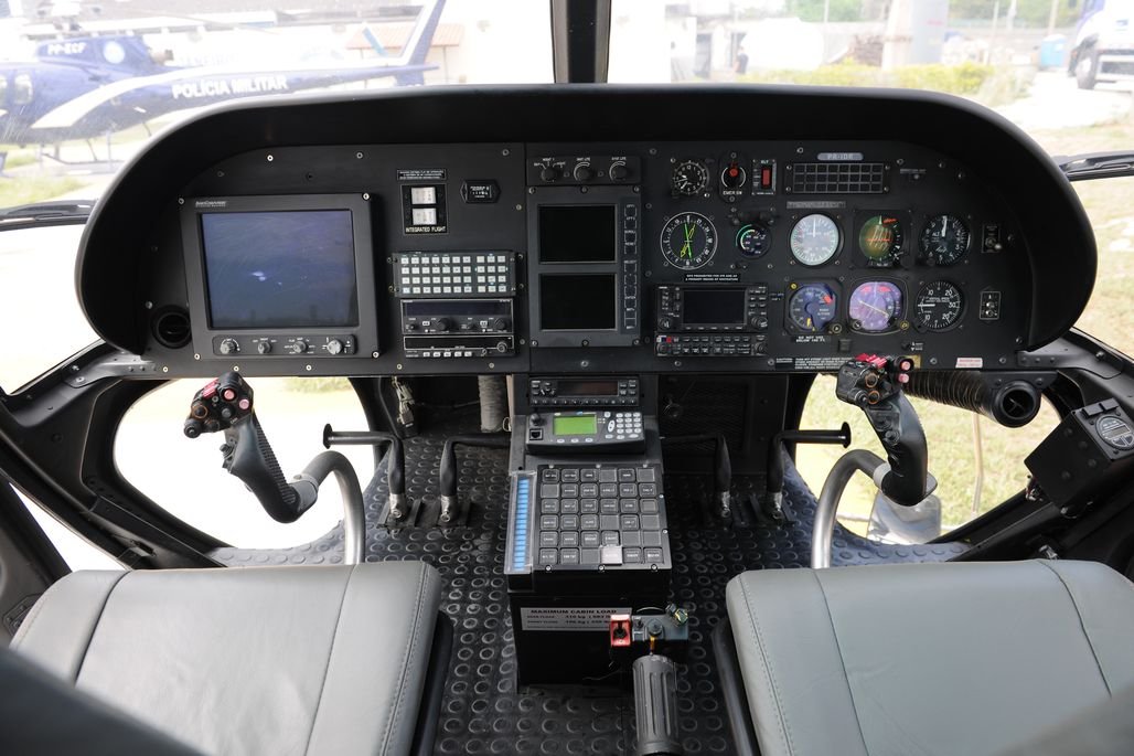 Interior cockpit view of Airbus AS350 Helicopter with various control panels, screens, and instrument gauges, along with pilot seats and control sticks.
