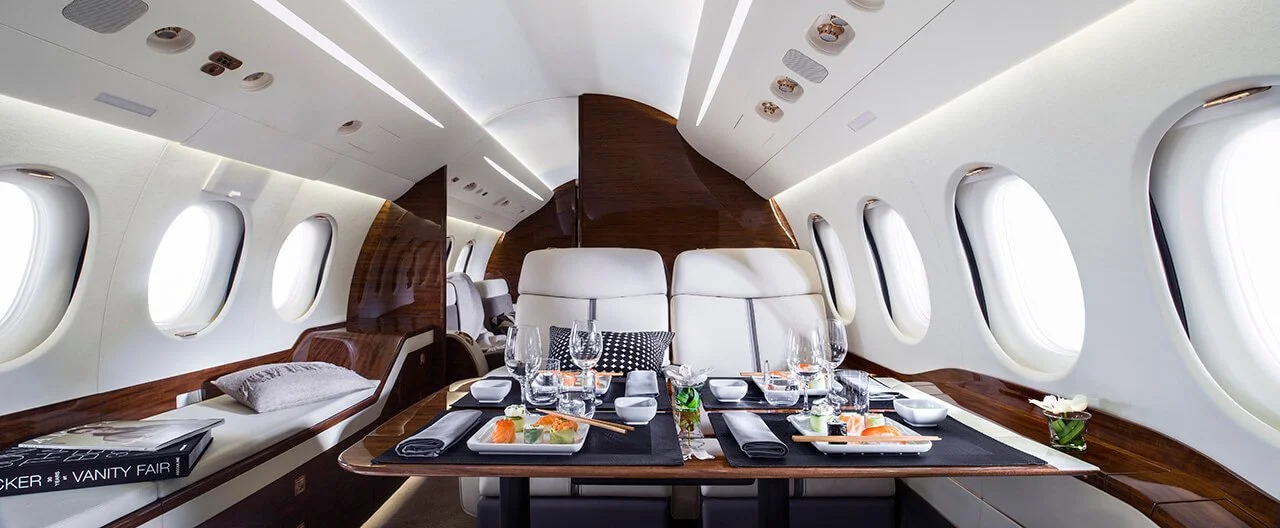 Luxurious private jet interior with dining table set, white leather seats, and large windows.