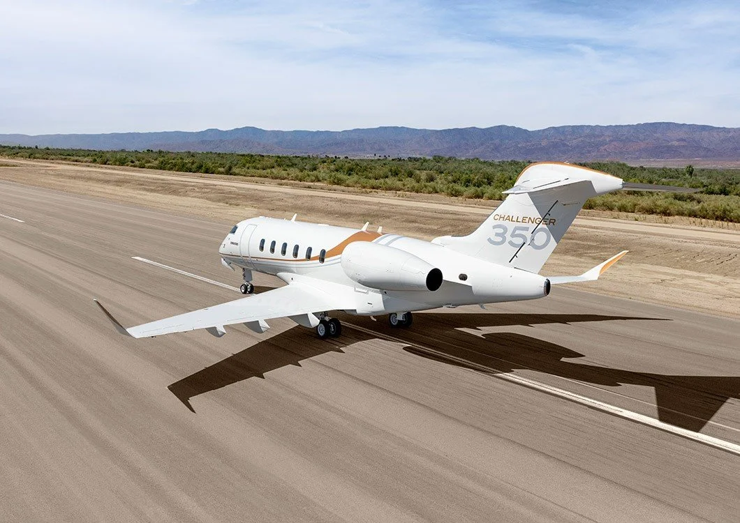Private jet Challenger 350 on airport runway with mountains in the background.