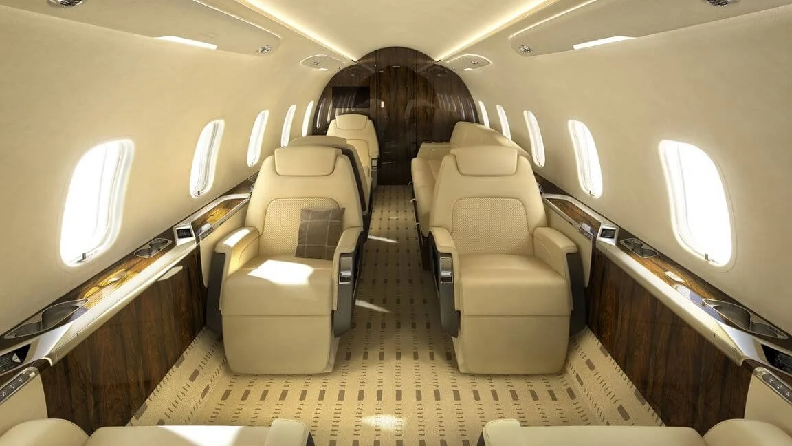 Interior of a luxurious Bombardier Challenger 350  with cream-colored leather seats and wood paneling.