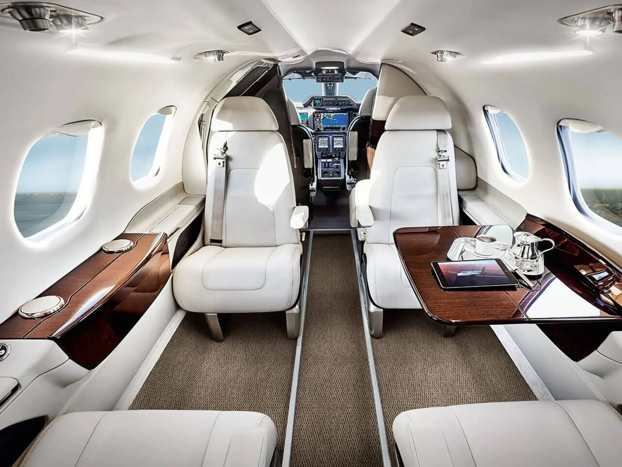 Embraer Phenom 100 Charter interior with leather seats, wooden cabinets, and a table. Cockpit visible at the front.