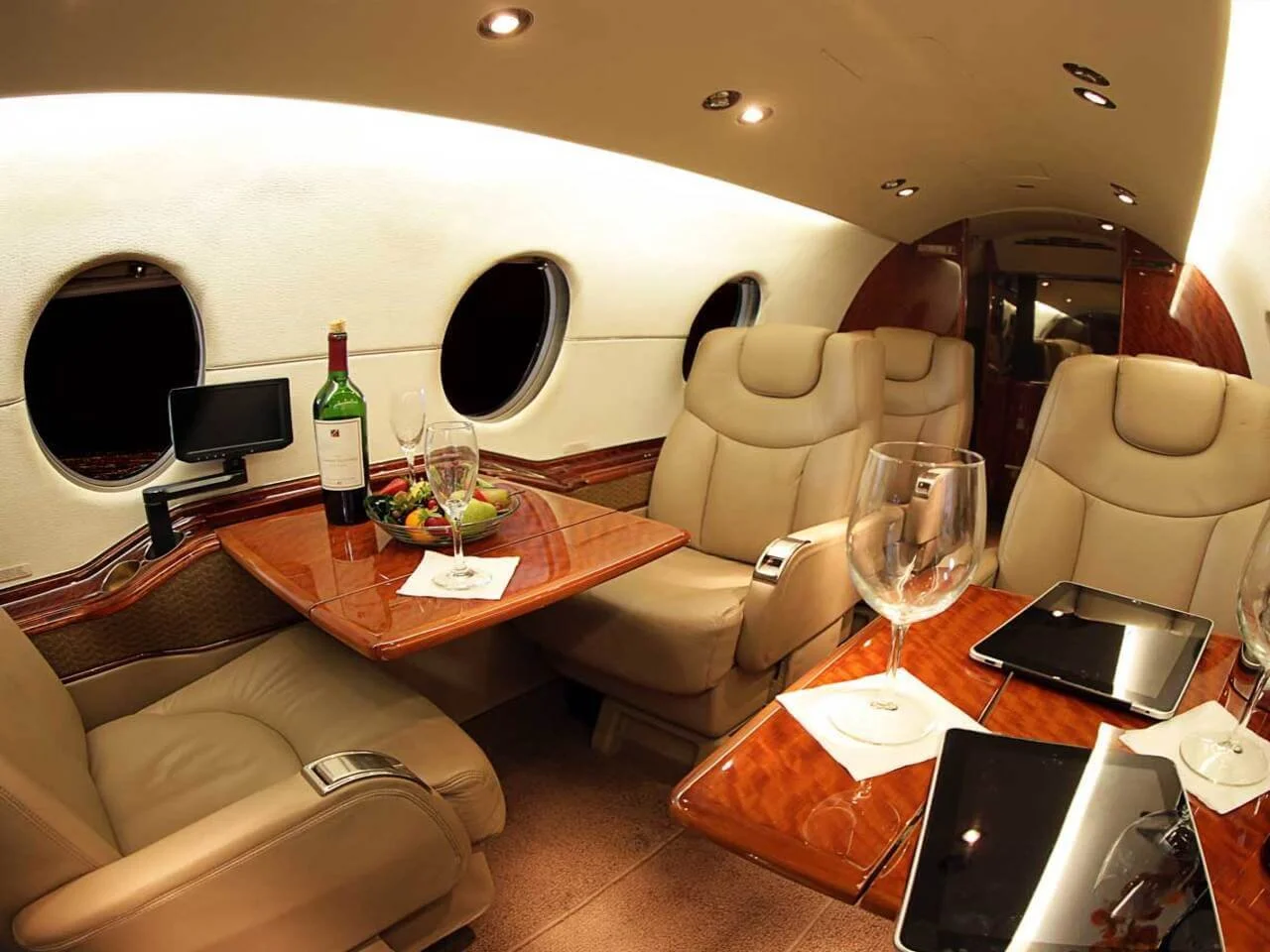 Interior of Hawker 400XP – Light Jet Charter
 with leather seats, a wooden table, wine bottle, fruit platter, glasses, and tablets.