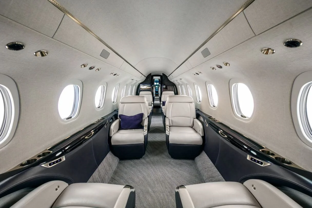 Interior of a luxury private jet Cessna Citation Longitude with beige leather seats and windows on both sides.
