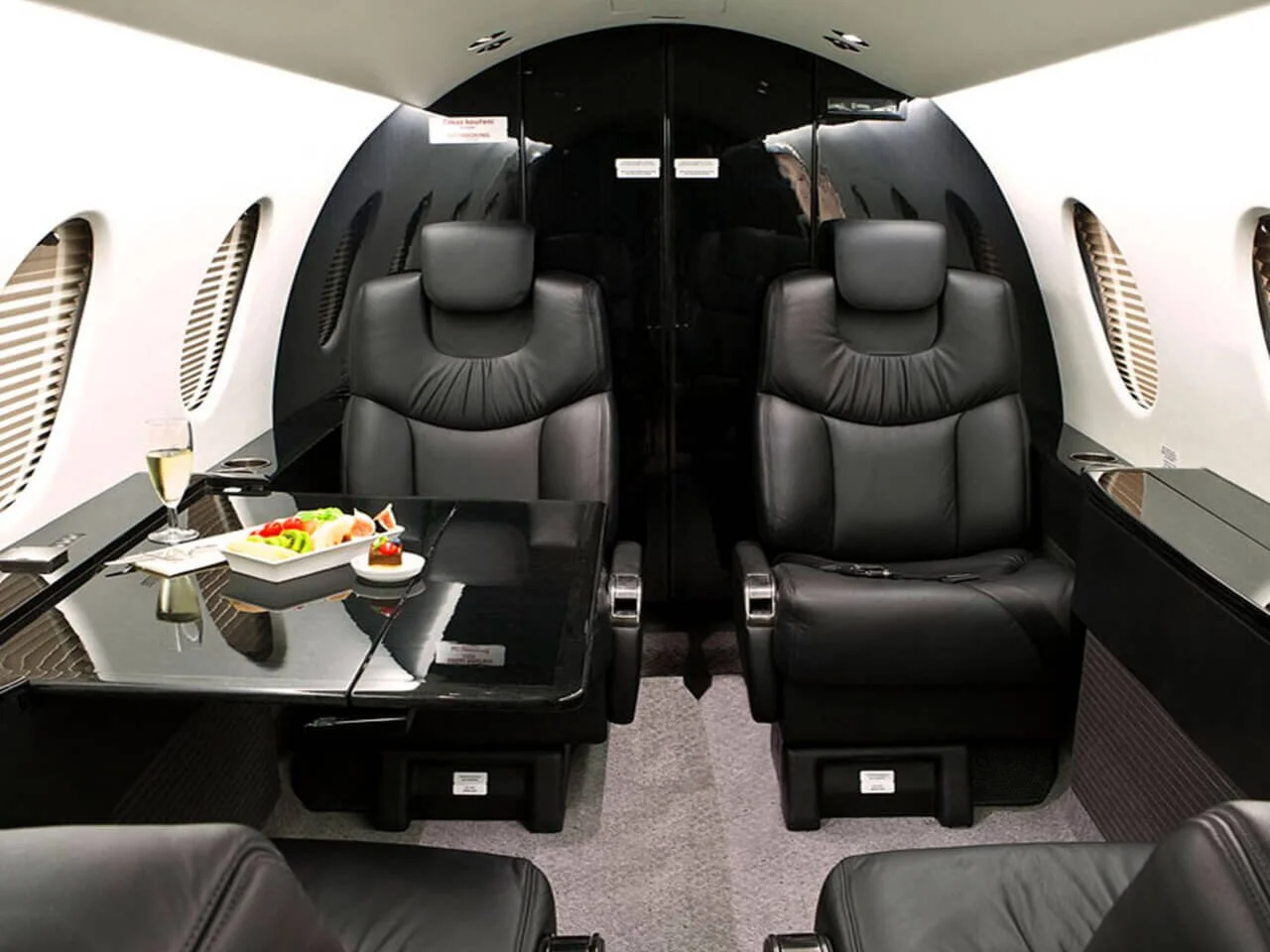 Interior of Nextant 400XT Light Jet featuring black leather seats, a polished table with a gourmet meal and a glass of champagne.
