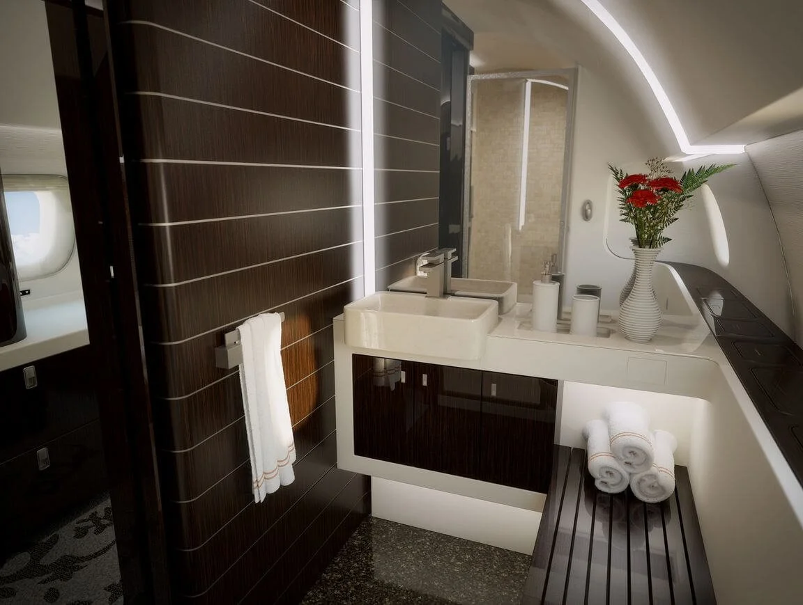 Luxurious airplane bathroom with dark wood paneling, a modern sink, rolled towels, and a vase of red flowers.