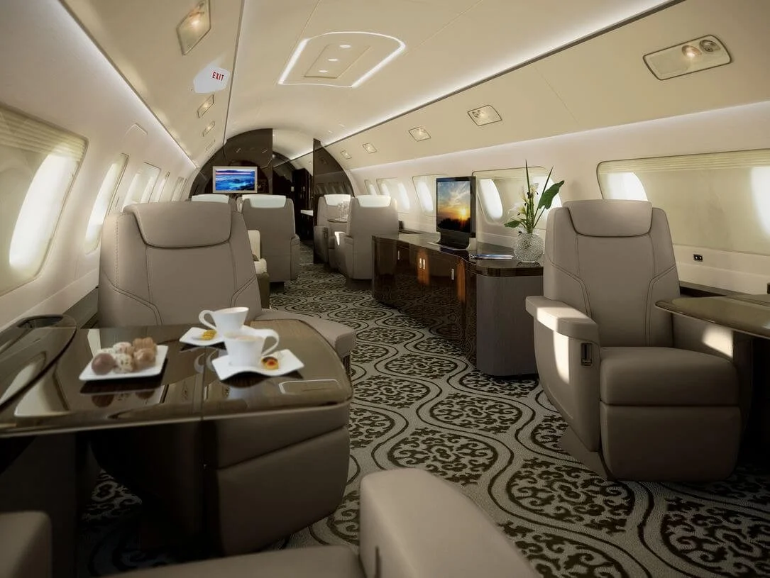 Luxurious private jet interior with plush seating, elegant décor, and a patterned carpet. Tables show tea cups and pastries, with a TV and flowers in the background. Ambient lighting creates a sophisticated atmosphere.