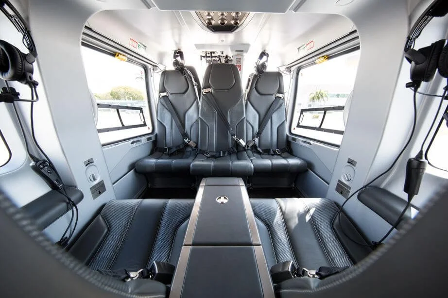 Interior of Airbus EC135 Helicopter Private Charter cabin with black leather seating and seatbelts.