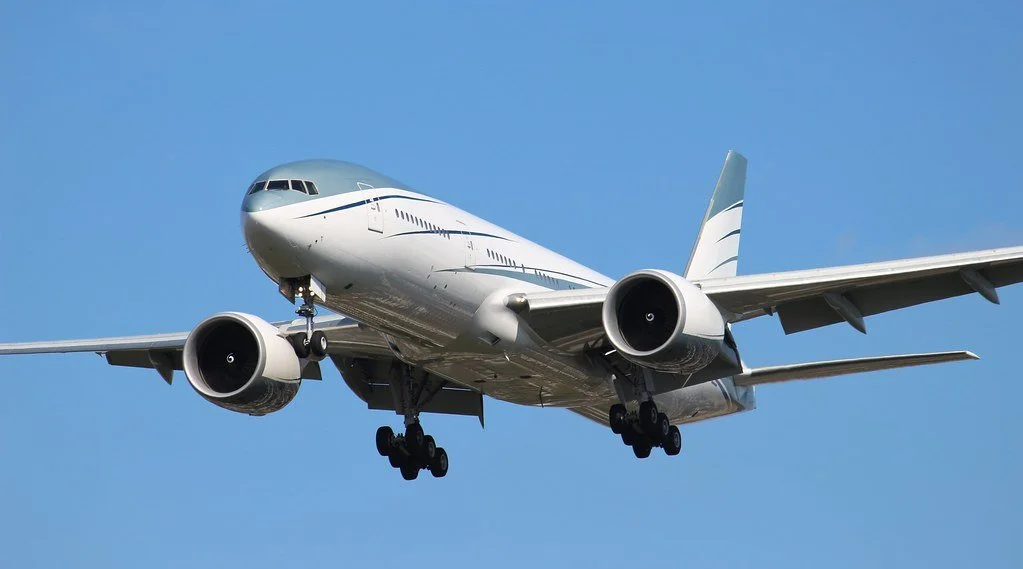 Commercial airplane in flight with landing gear deployed against a blue sky.