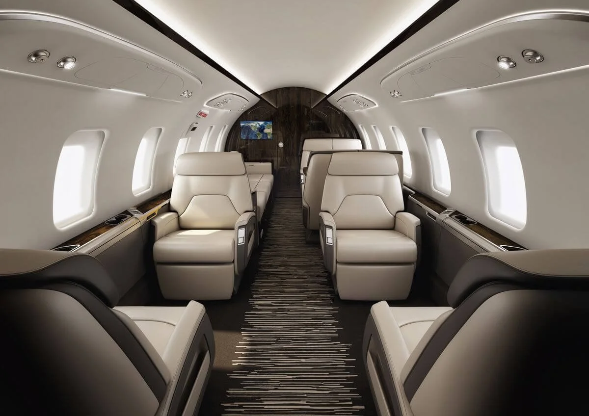 Luxurious Bombardier Challenger 650 Large Jet with beige leather seats, overhead compartments, and modern lighting.