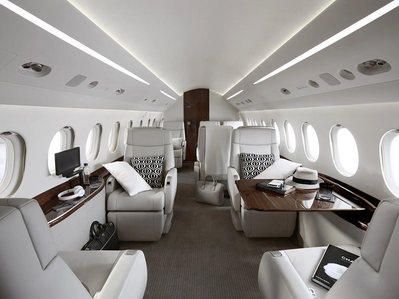Dassault Falcon 2000LX – Efficient Twin-Engine Business Jet interior with leather seating, wood tables, pillows, and personal items like a hat, headphones, and a magazine.
