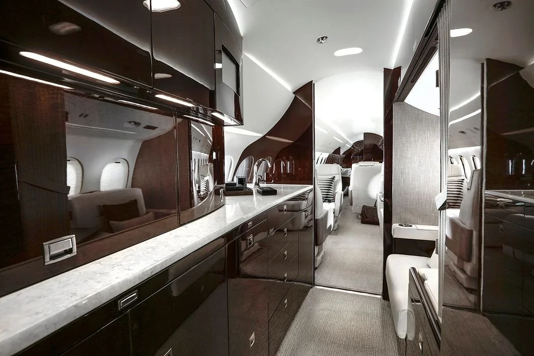 Interior of a luxury private jet with a modern kitchen area, glossy cabinets, and seating area with plush chairs.
