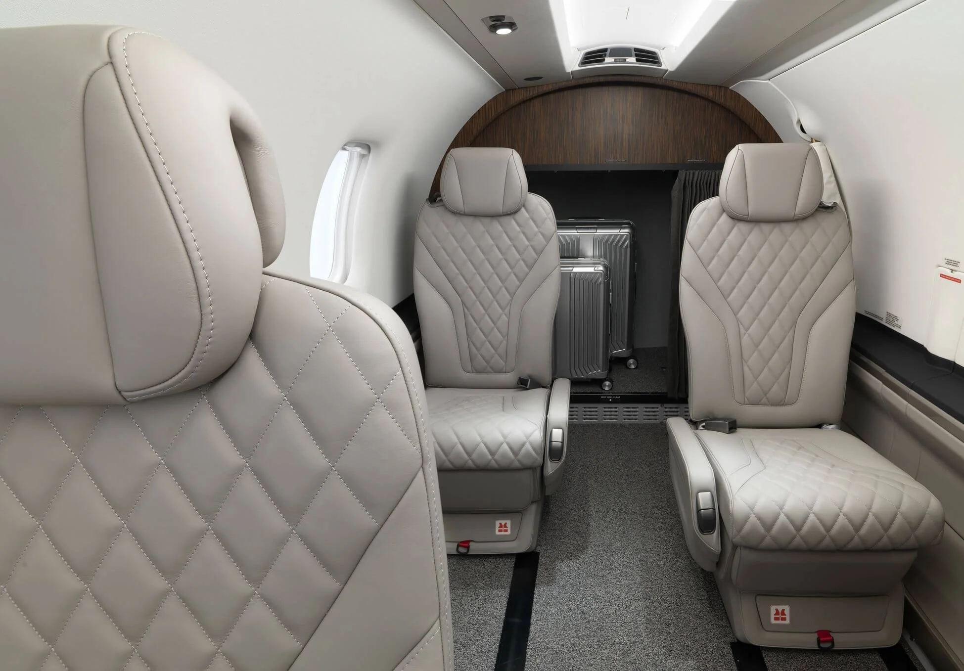 Interior of a private jet with beige leather seats and quilted pattern, featuring overhead lighting and luggage storage at the back.