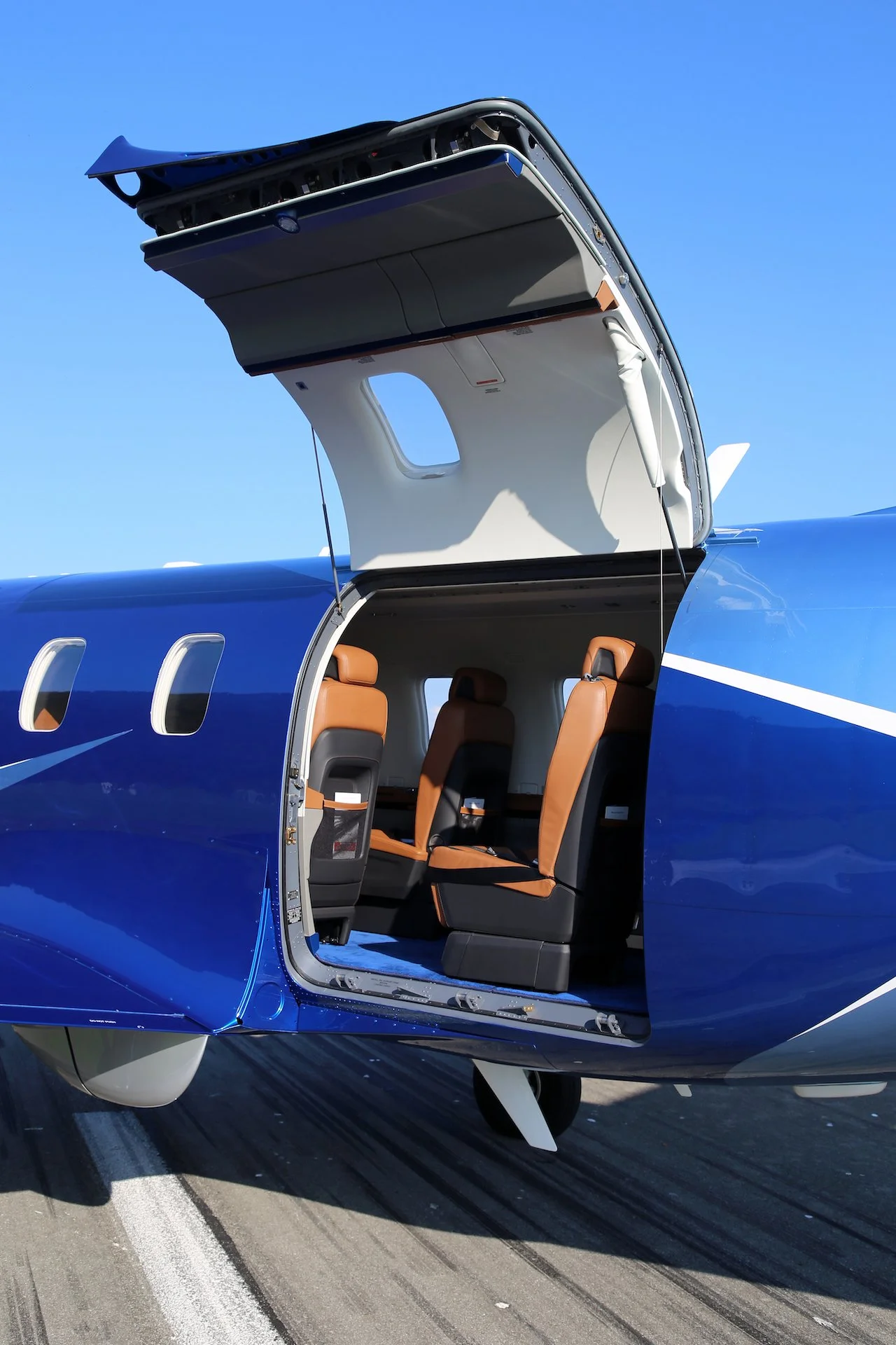 Open door of a small private jet revealing leather seats with a blue exterior against a clear sky.