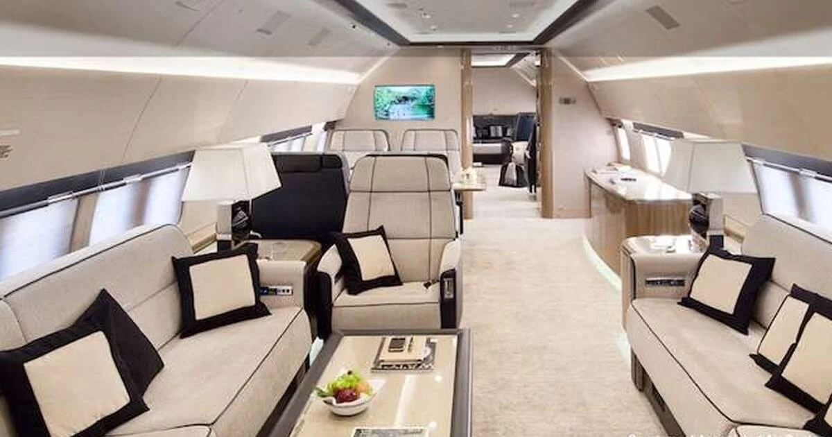 Luxury private jet interior with beige seating, pillows, and elegant lighting.