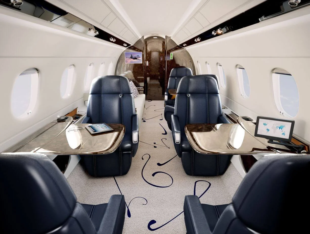 Interior of a private jet with luxurious blue leather seats, foldable tables, and windows. The cabin is spacious, featuring a carpet with elegant design, two digital tablets on tables, and a decorative picture on the wall.