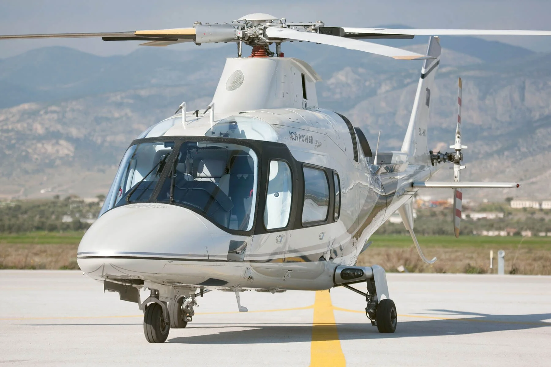 Front view of a white Agusta A109 Helicopter
 on a runway with mountains in the background.