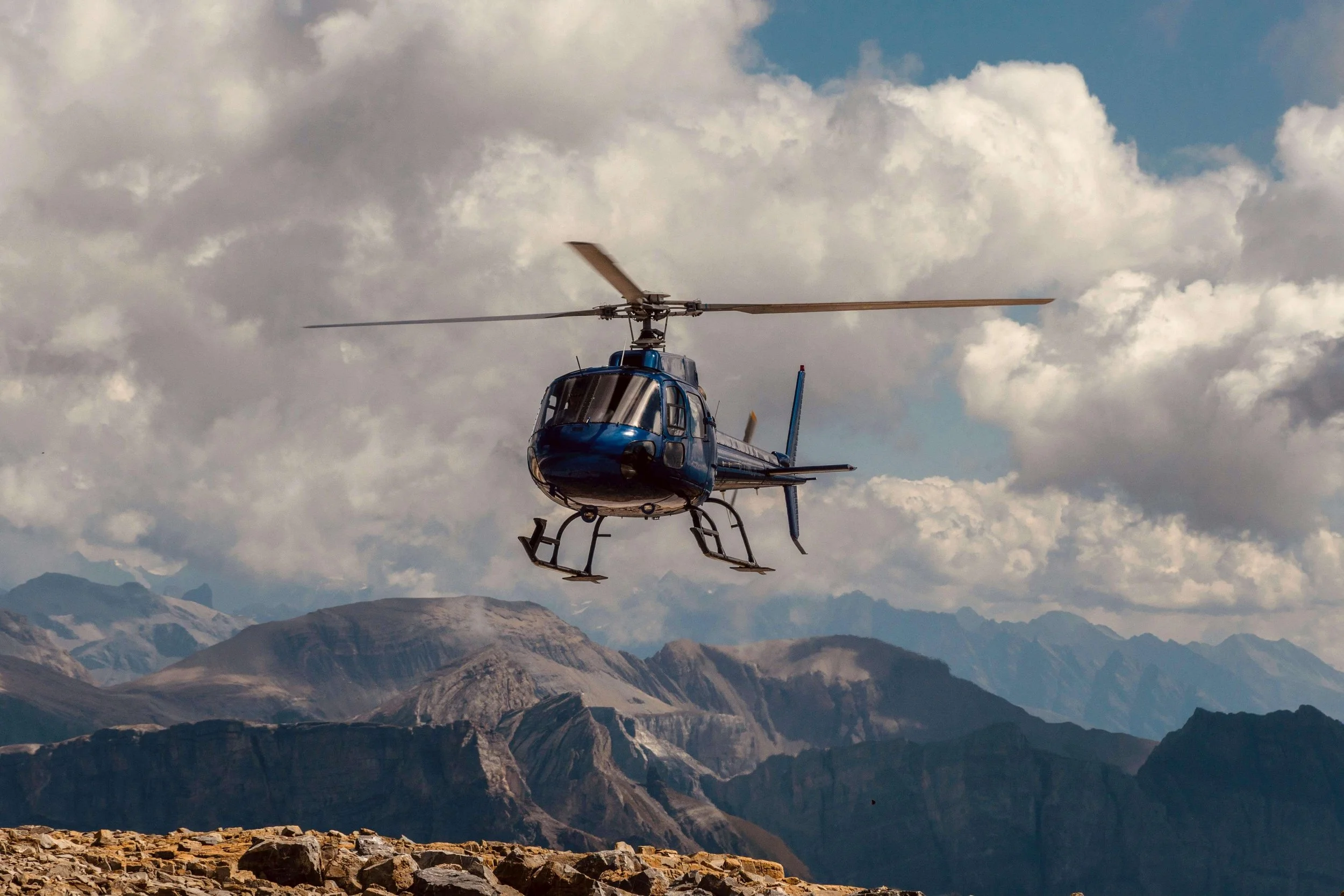 Helicopter Charter - Blue helicopter flying over mountainous landscape under cloudy sky.