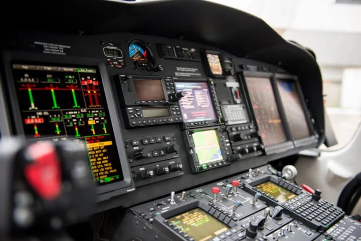 Interior view of an aircraft cockpit with various digital flight instruments and control panels.