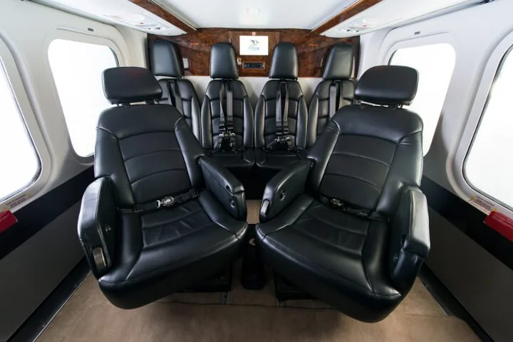 Interior of a luxury helicopter with black leather seats arranged in two rows, facing each other, and large windows on the sides.