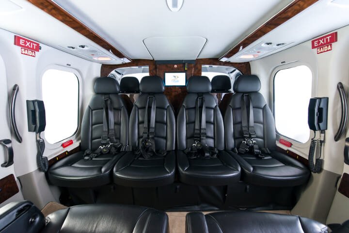 Interior of Agusta A139 helicopter with black leather seats facing forward, seat belts, and windows on the sides. Exit signs are visible above the windows.