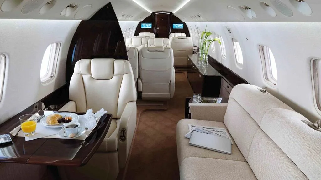 Interior of Embraer Legacy 600 – Long-Range Luxury Jet Charter
featuring beige leather seats, a table set with breakfast, soft lighting, and elegant decor.