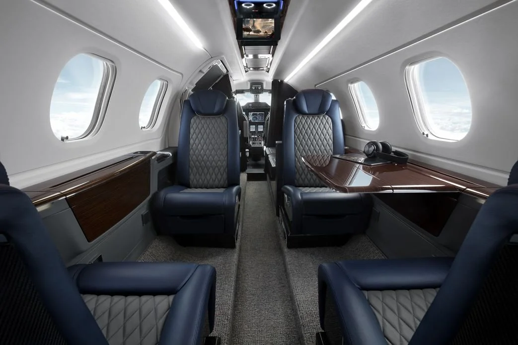 Embraer Phenom 300 – Light Jet Charter interior with plush leather seats, wooden tables, and windows with views of clouds.