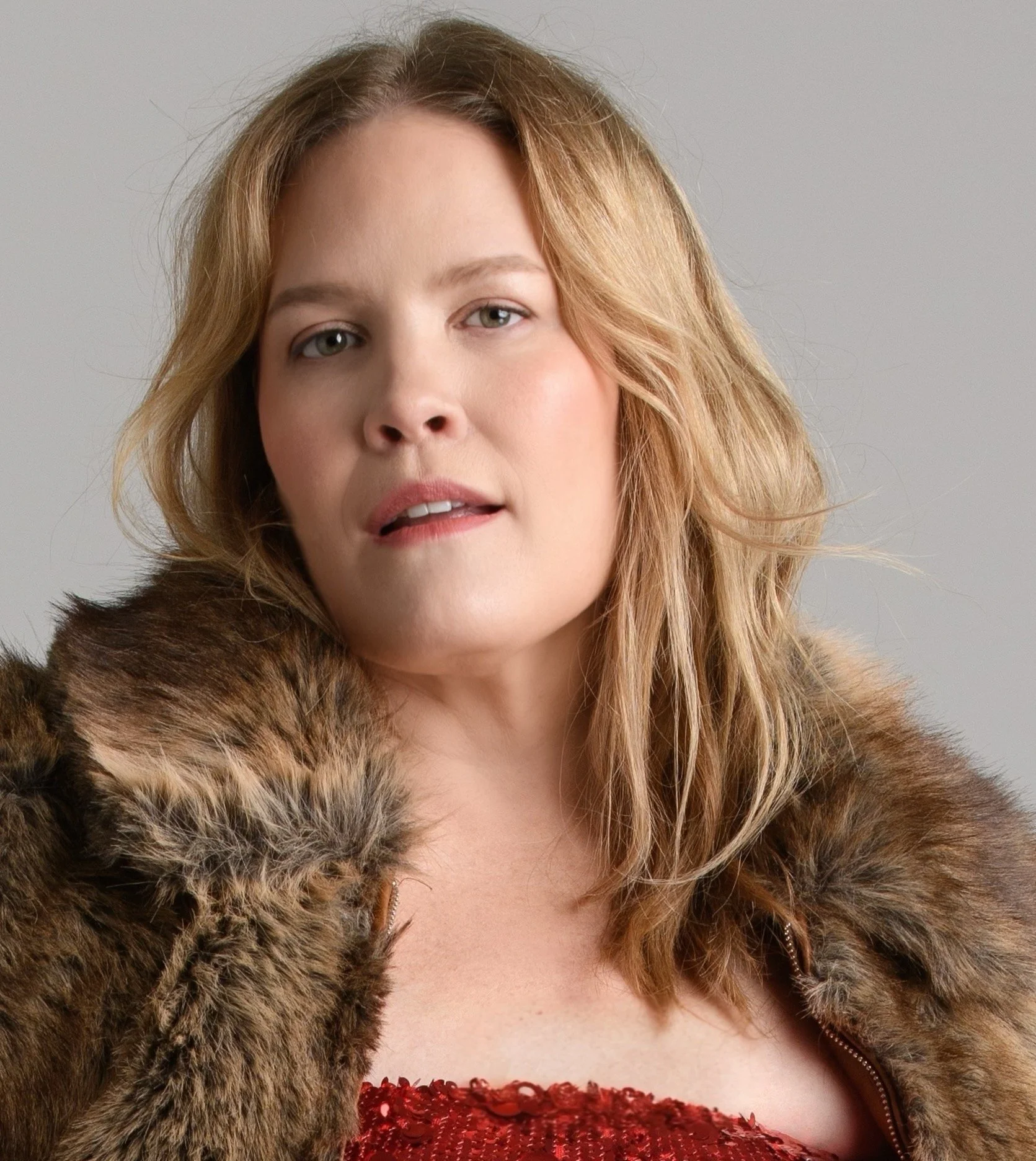 A woman with shoulder-length blonde hair wearing a brown fur coat and a red sequined dress.