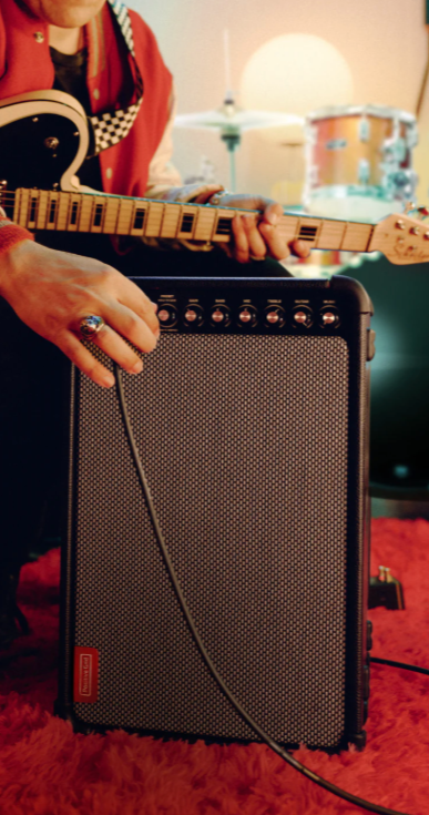 Close-up of a person adjusting a guitar amplifier with a guitar in the background.