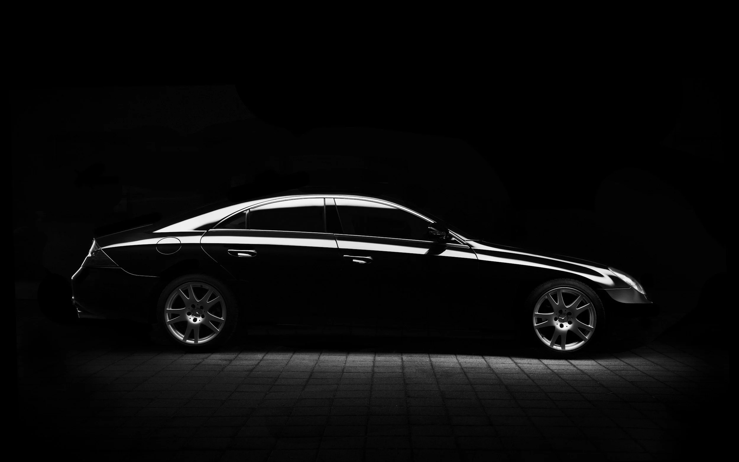 A sleek black luxury car with silver rims, illuminated in a dark setting with reflected light lines on its surface.