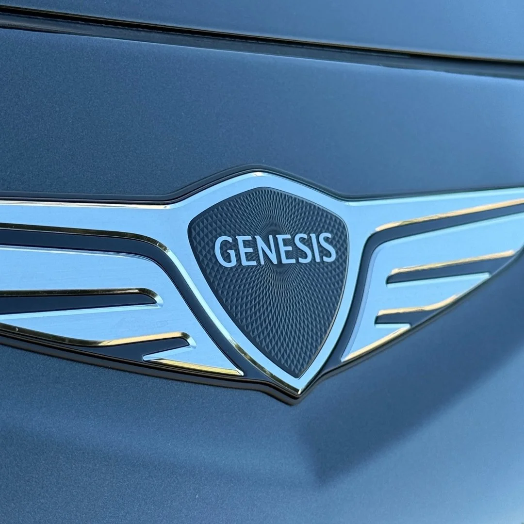 Close-up of a Genesis logo on a vehicle with metallic blue paint.
