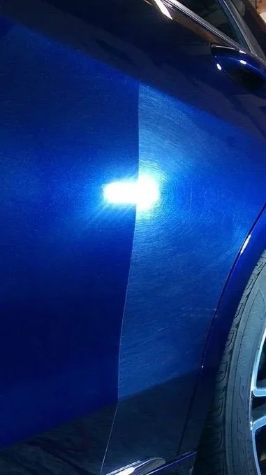 Close-up of a blue car door with a bright reflection of a light source.