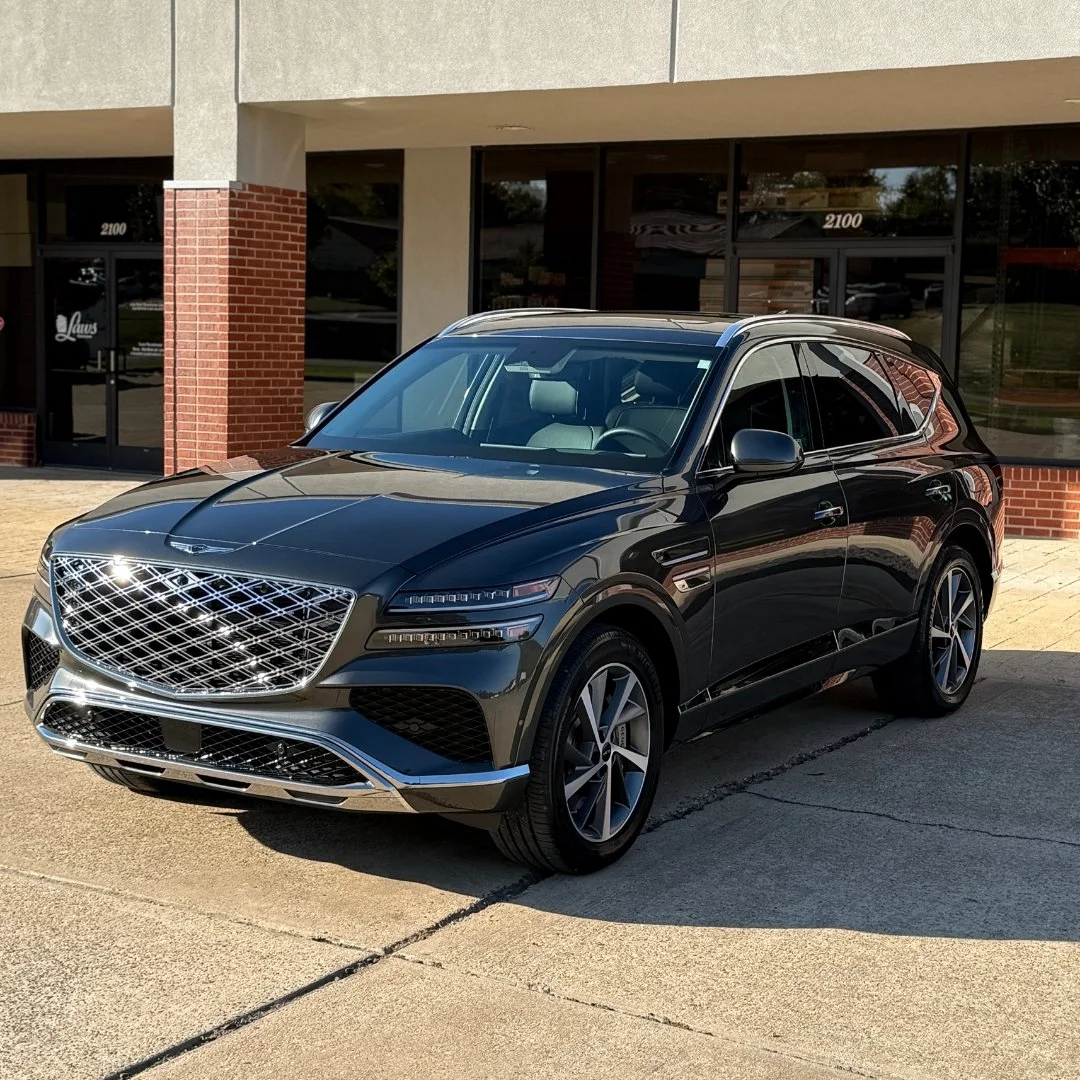 A black luxury SUV parked outside a commercial building with glass windows and a brick wall.