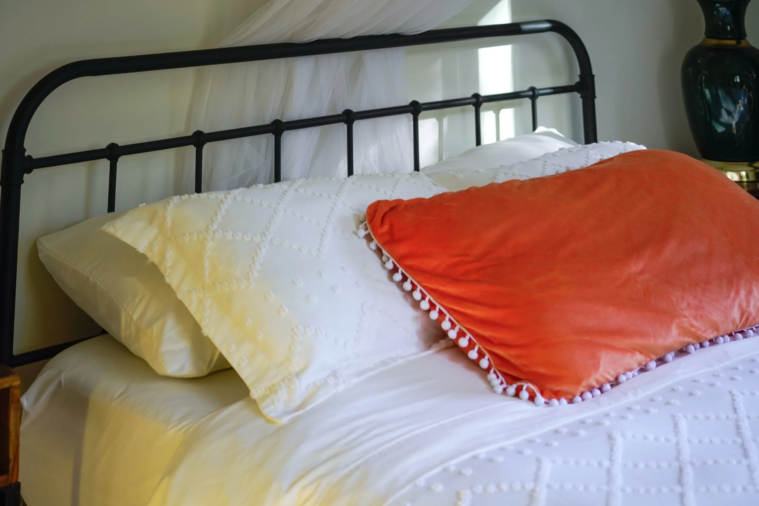 Soft white bedding and an orange velvet pillow on the queen bed at Blossom Sanctuary, an intimate wellness retreat in Etna, California
