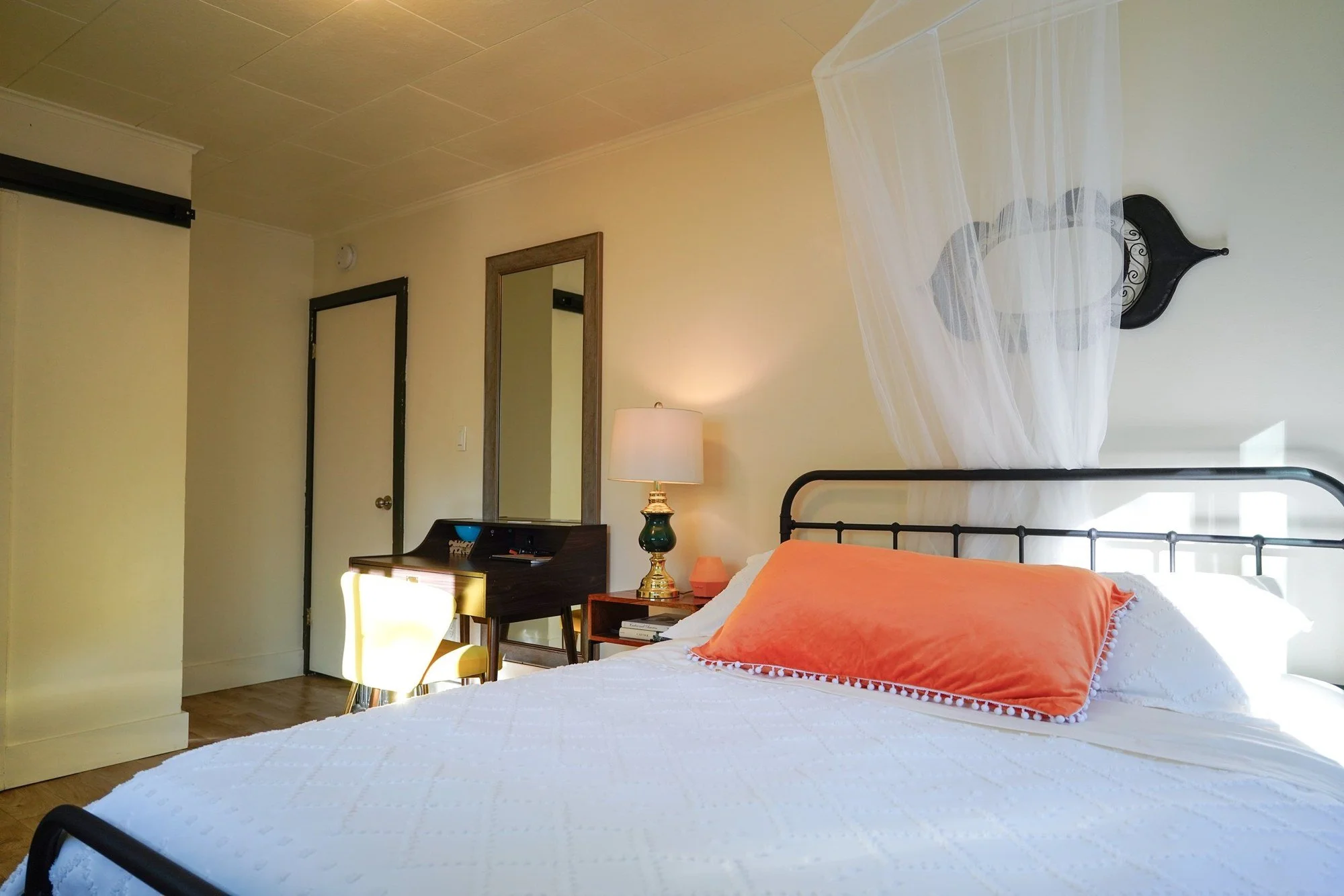 The queen bedroom at Blossom Sanctuary: white bedding, a coral velvet pillow, an iron bed frame and a sheer canopy