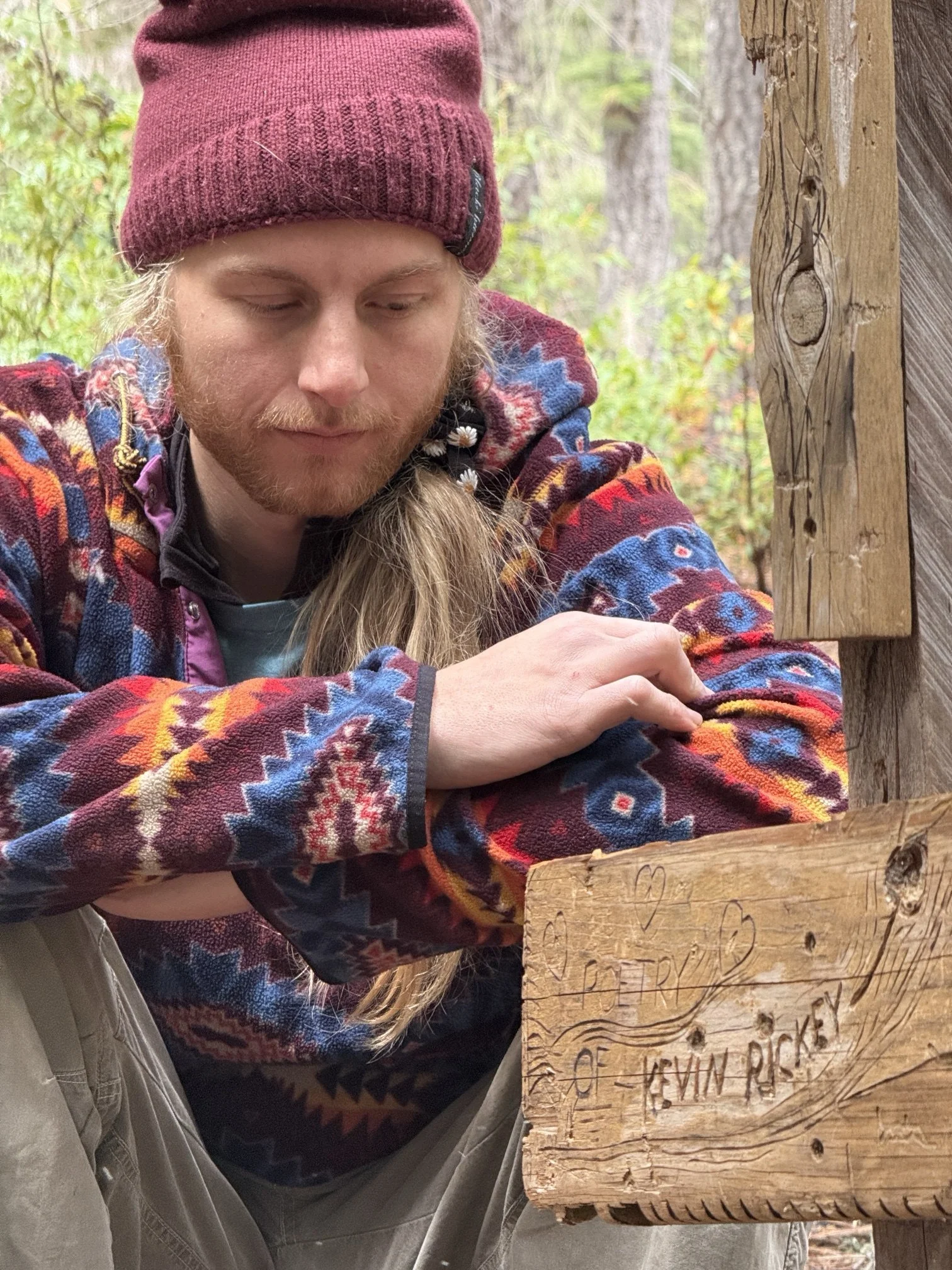 Colt sitting beside a hand-carved wooden sign that reads "Poetry of Kevin Rickey"