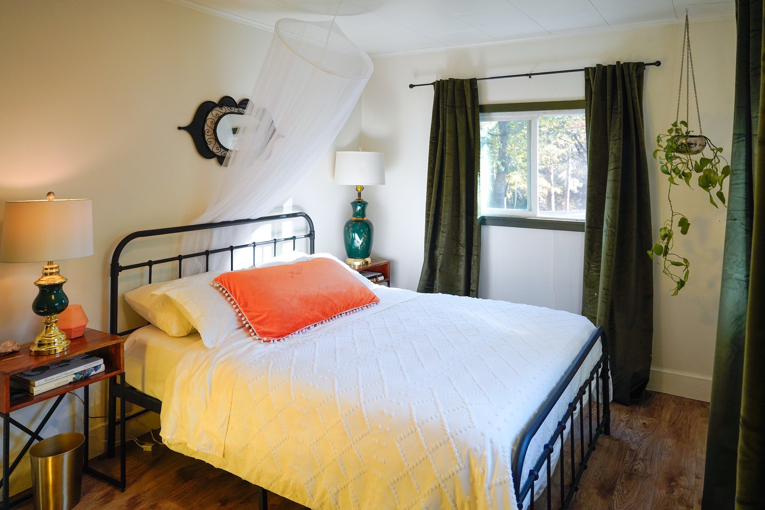 Queen bedroom with a black iron bed, a sheer canopy, an orange velvet pillow and green velvet curtains