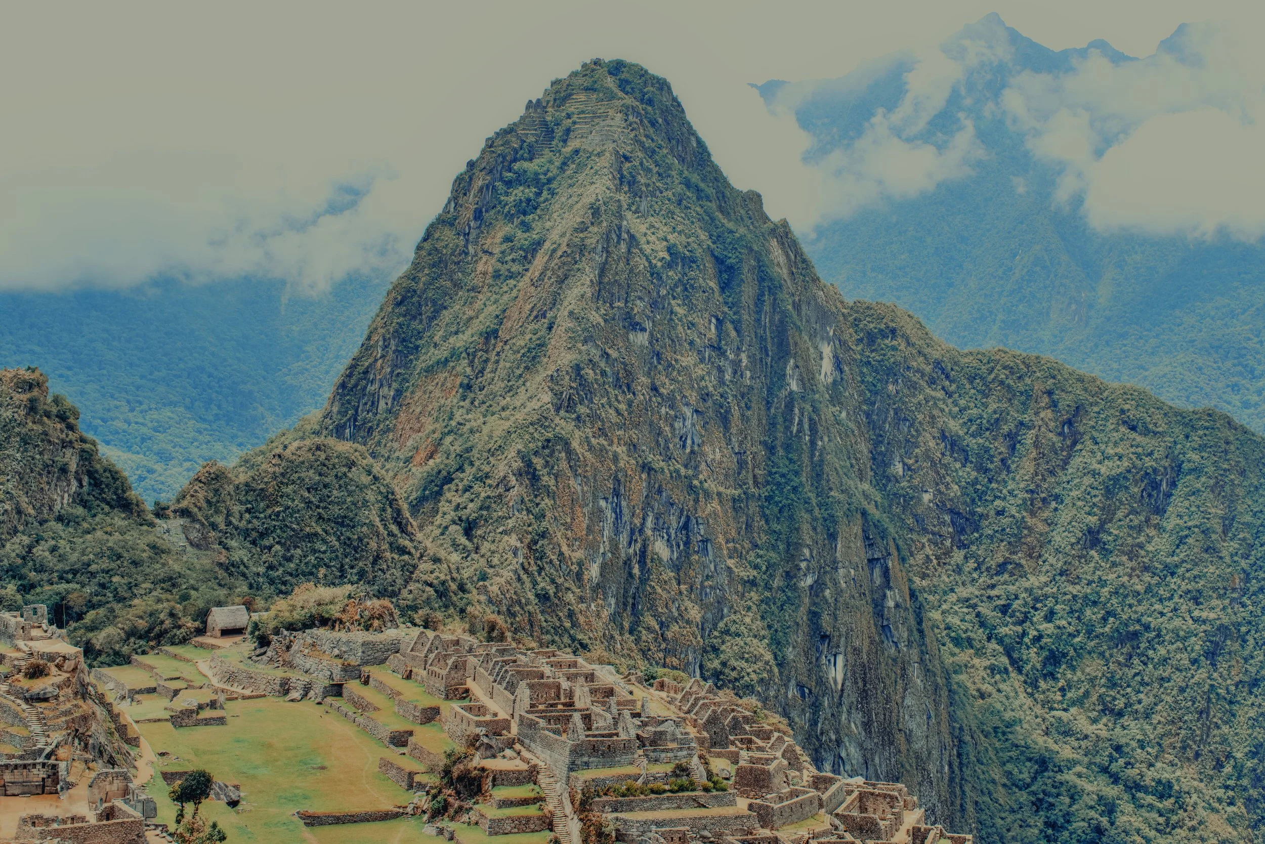 View of Machu Picchu in the mountains with lush greenery and overcast sky.