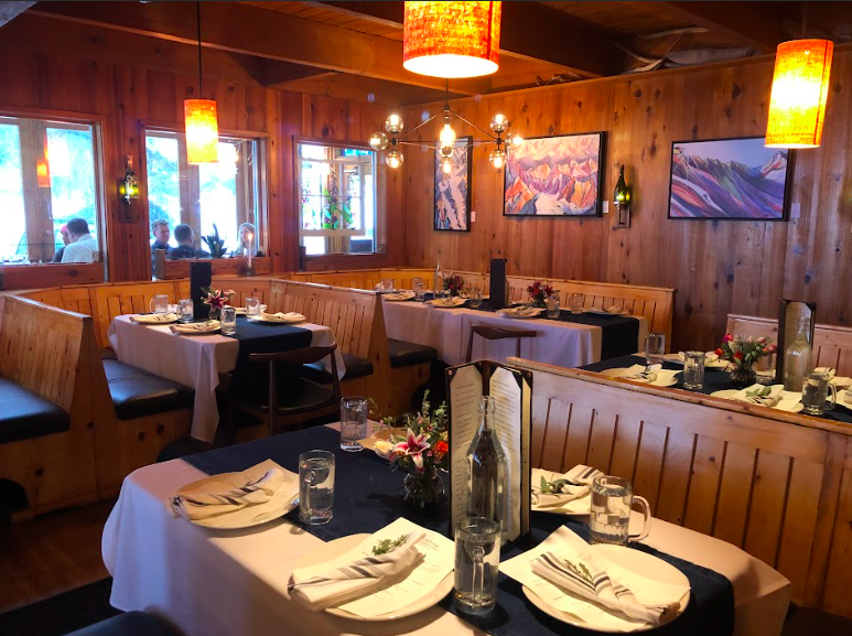 Interior of a cozy restaurant with wooden walls, decorated with landscape paintings, with warm lighting from hanging lamps. Corporate events, conference dinner space.  Company dinners, holiday parties. Alaska holiday parties.