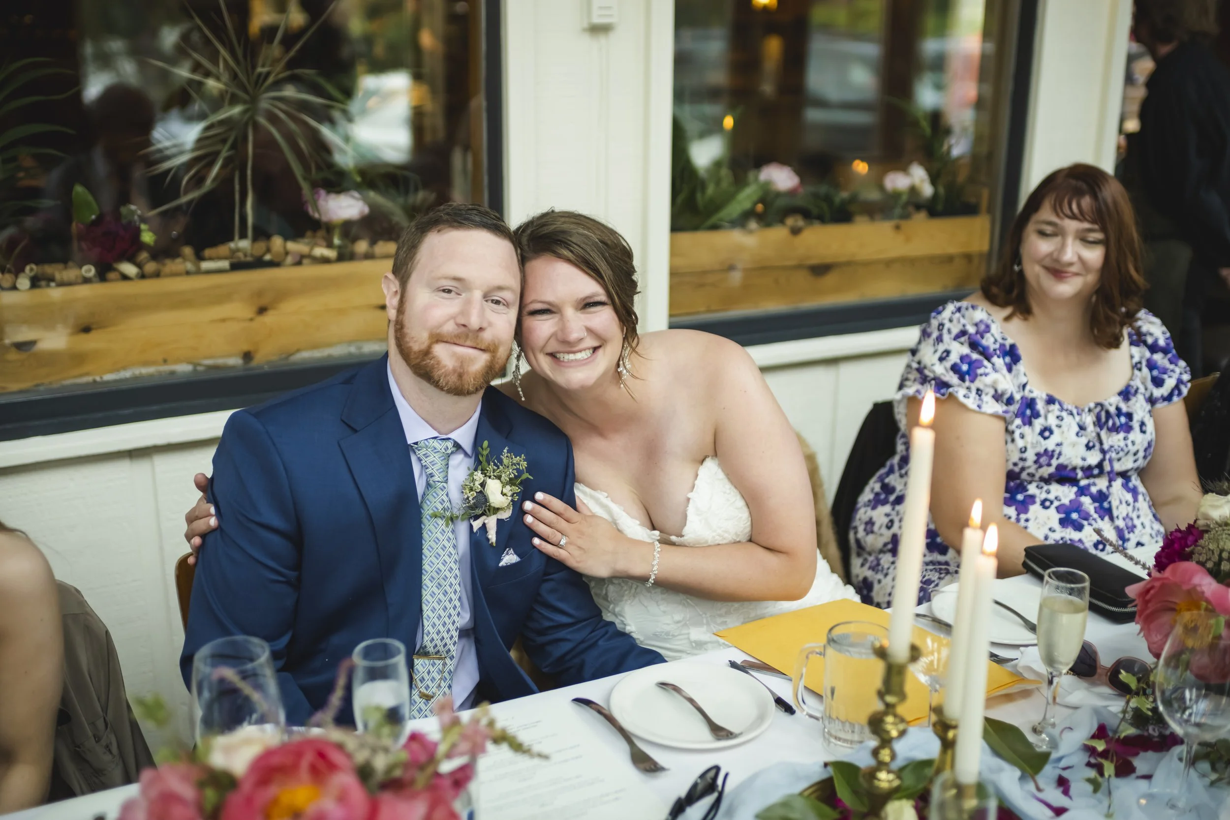 A smiling bride and groom sitting at their wedding reception table.  World famous architect celebrates her wedding with her ginger bo-hunk. 