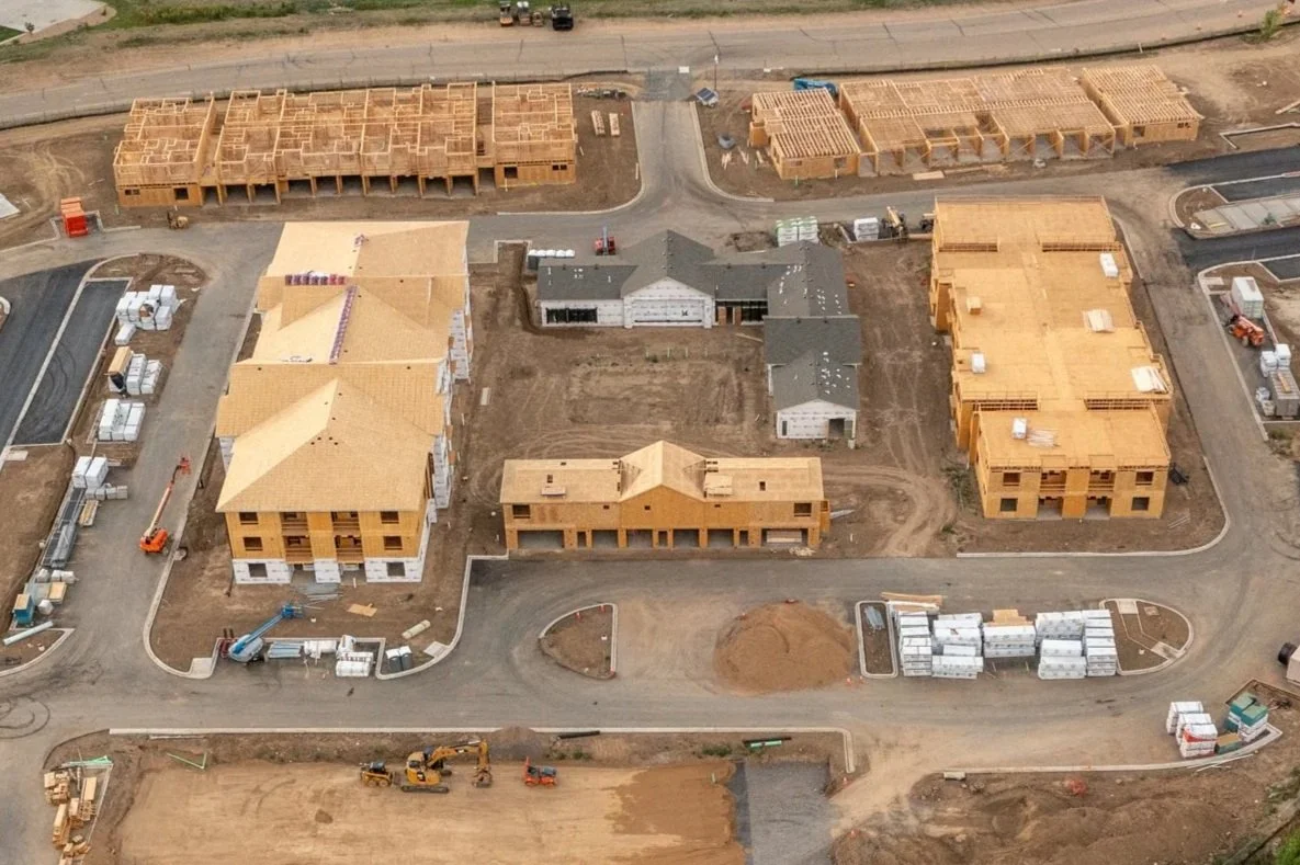 Aerial view of a construction site with multiple buildings in various stages of construction and surrounding paved roads.