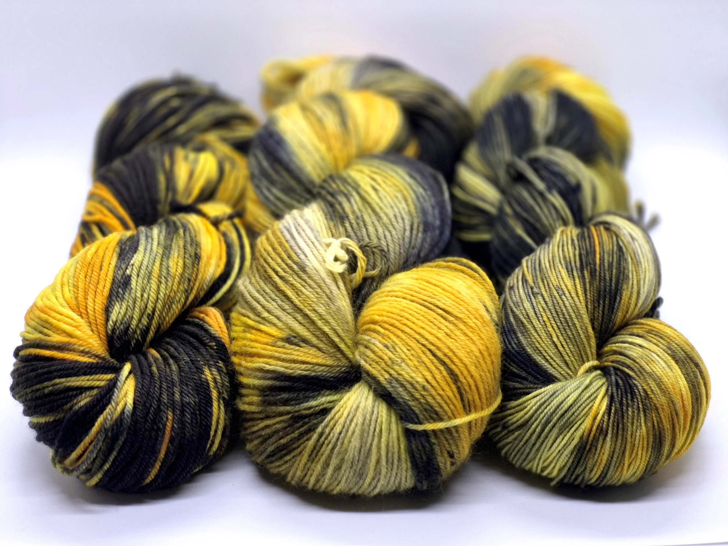Multiple skeins of yellow, black, and gray variegated yarn arranged on a white surface.