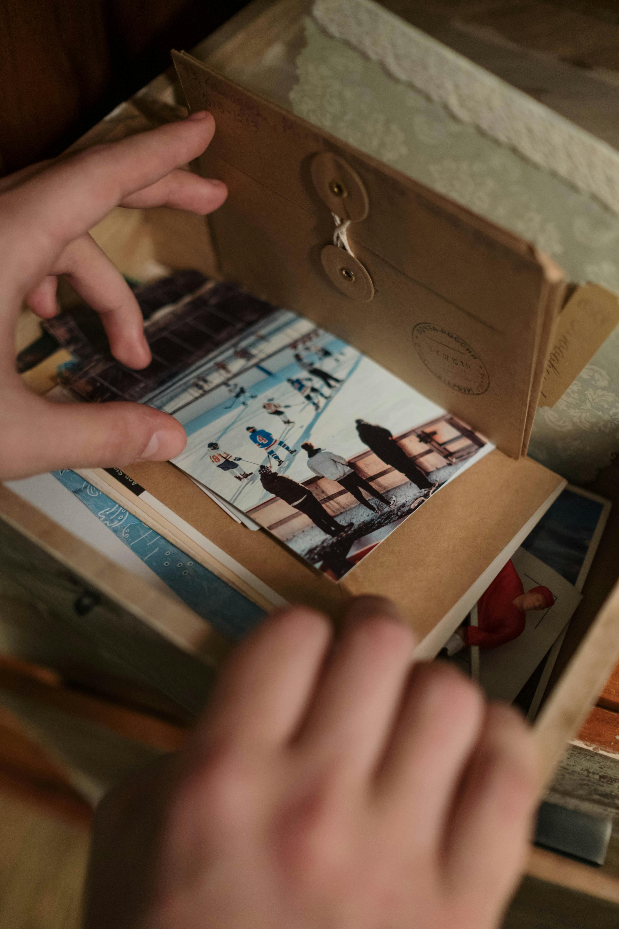 Two hands are flipping through printed photographs and memorabilia are in a photo box