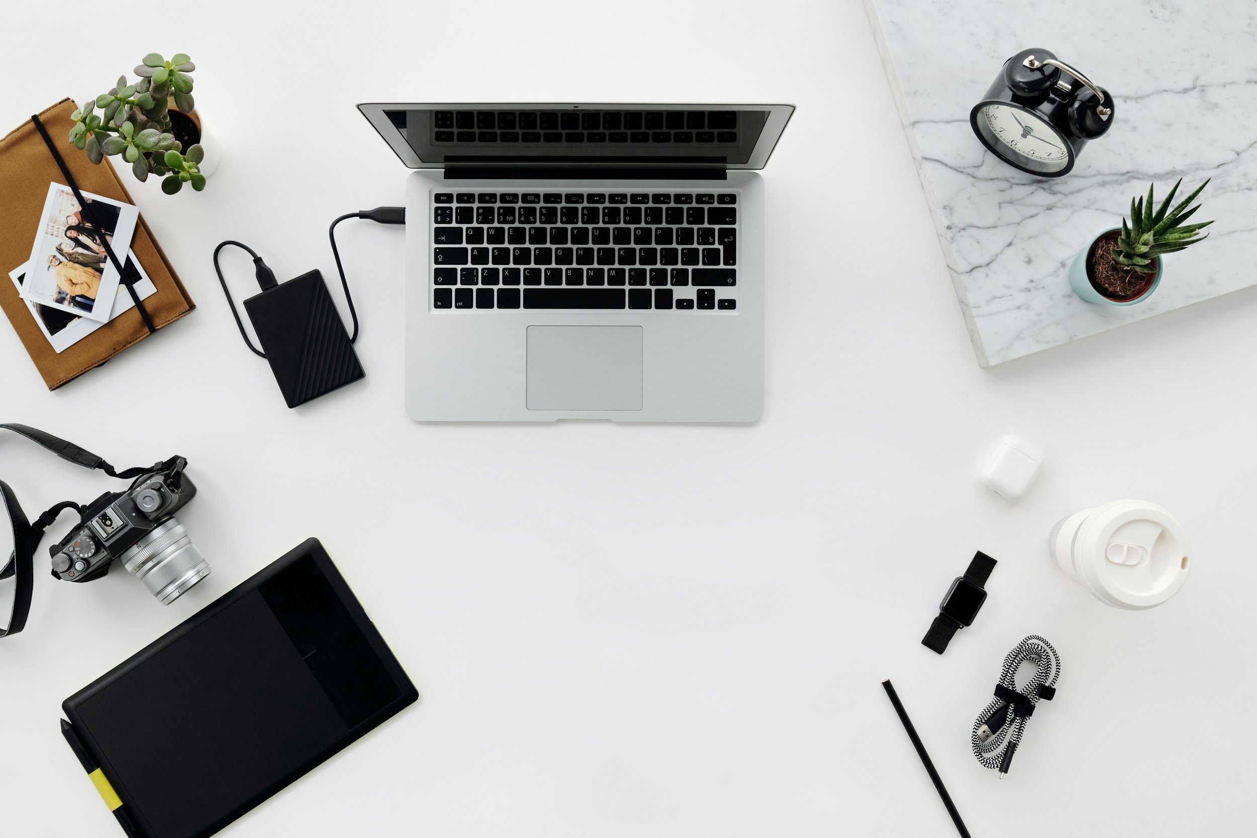 Desktop with photographs, notebook, plant, laptop, and external hard drive referencing digital organizing and saving to an EHD