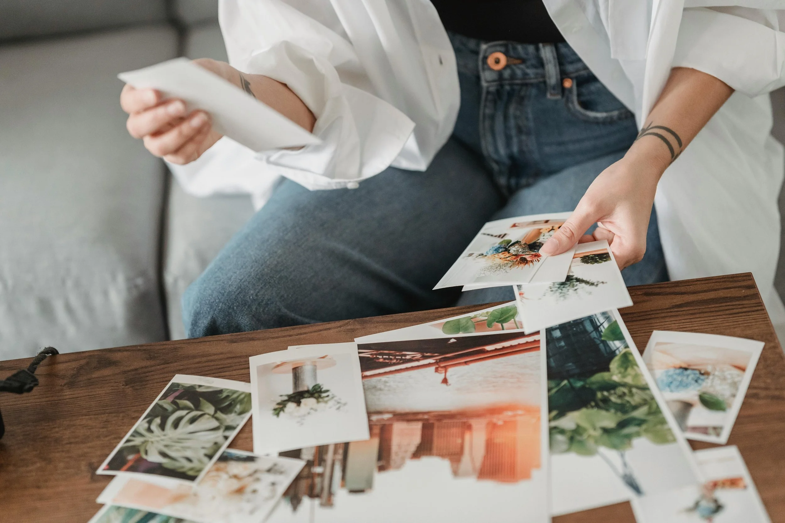 Lady is sitting on a couch with a table filled with different size printed photographs preparing them for printed photo organizing