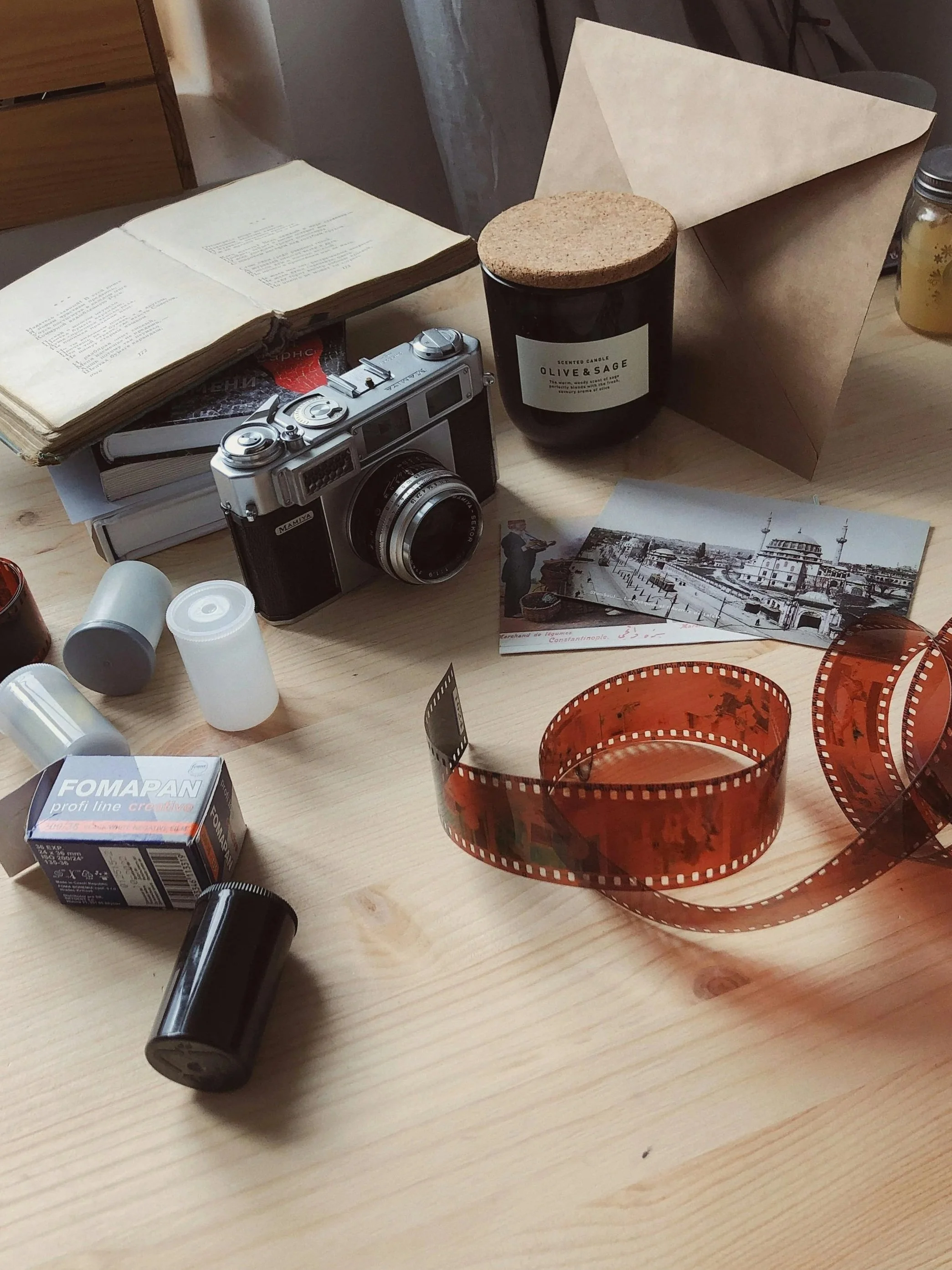 Camera, empty plastic film containers, photographs and a roll of negatives appear on a desk which need to be digitized to avoid further deterioration