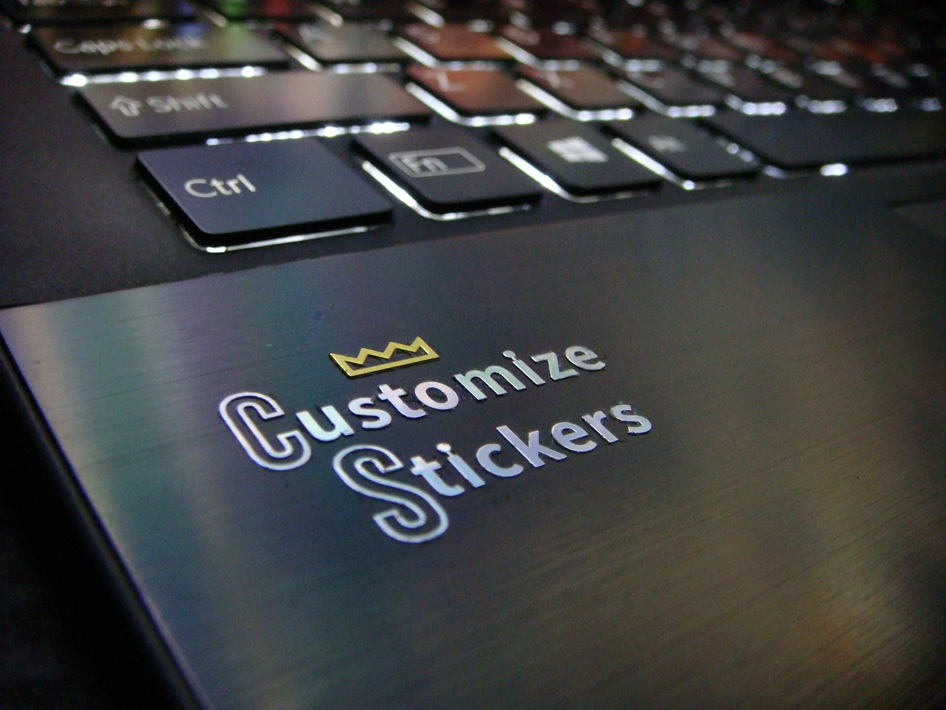 Close-up of a laptop keyboard with a sticker that reads 'Customize Stickers' and a small crown icon above the text.