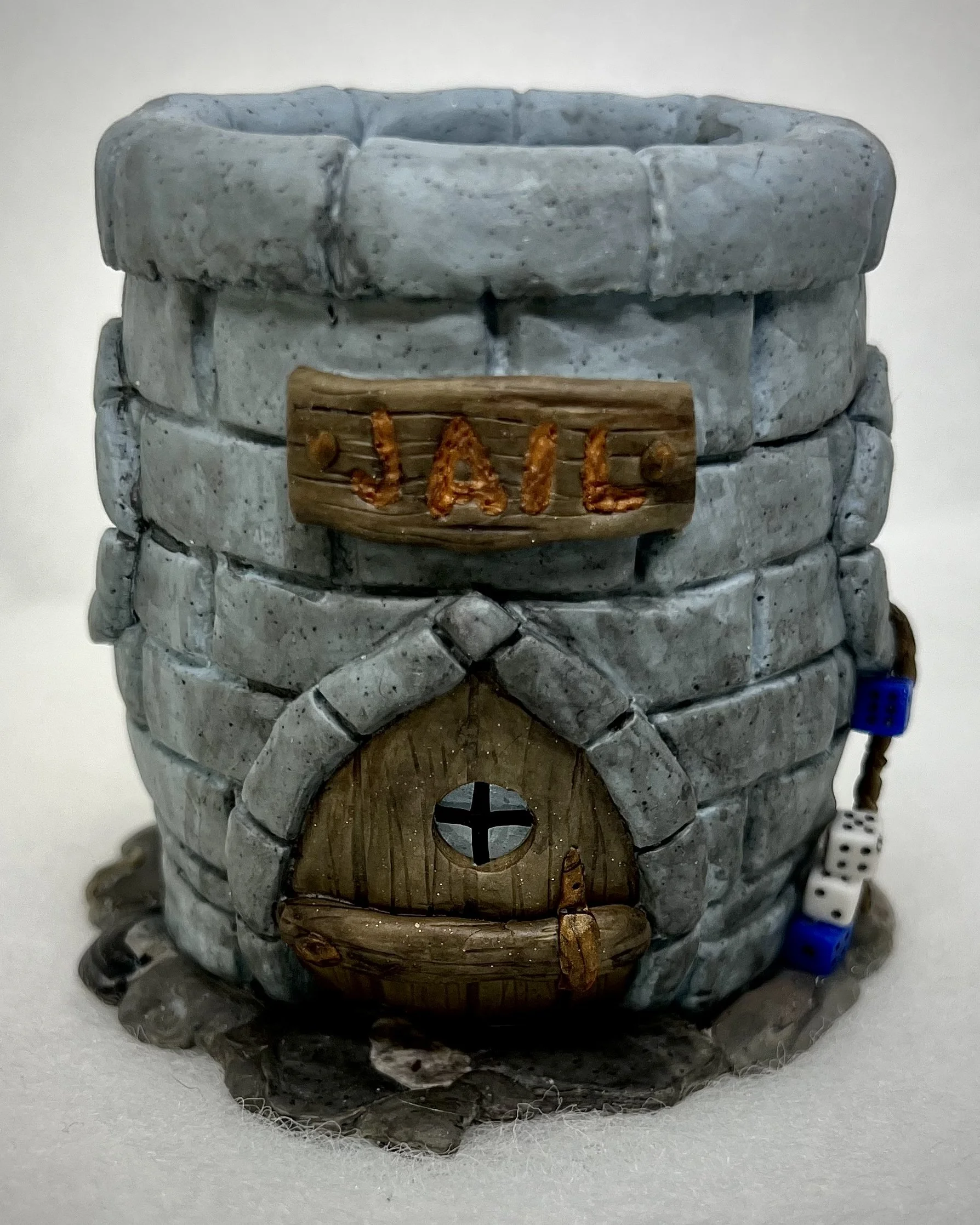 Miniature stone well with a wooden door, small circular window, and a baked clay sign that says 'JAIL' in front.